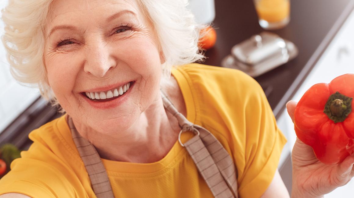 Uśmiechnięta, siwowłosa pani trzyma paprykę