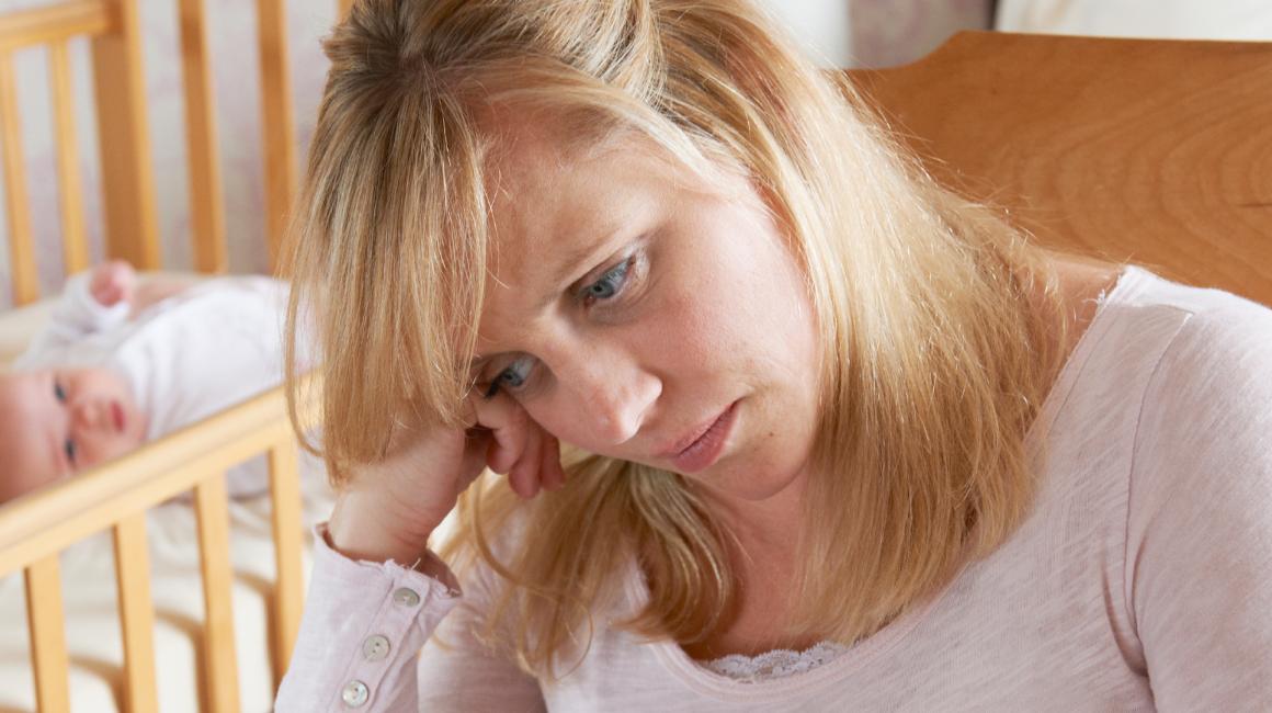 Smutna matka, w tle niemowlę w łóżeczku