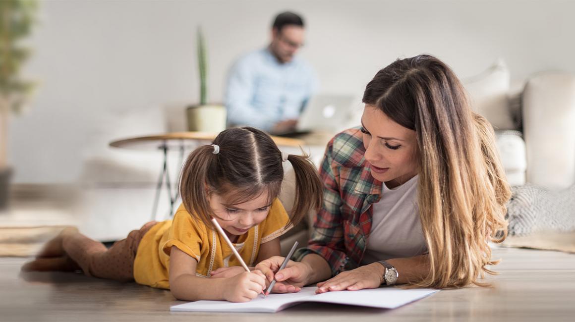 Córka rysuje, matka leży obok, w tle ojciec z komputerem