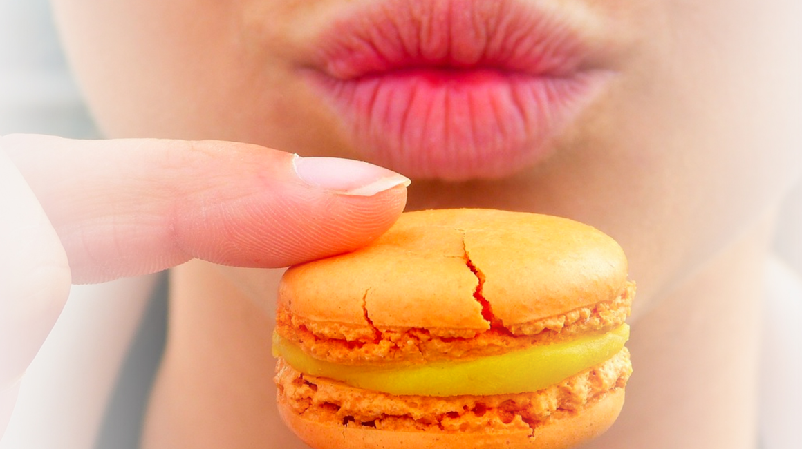 Widok dolnej części twarzy i ciasta przed nią trzymanego dwoma pacami prawej ręki. Ciastko z nadzieniem w środku.