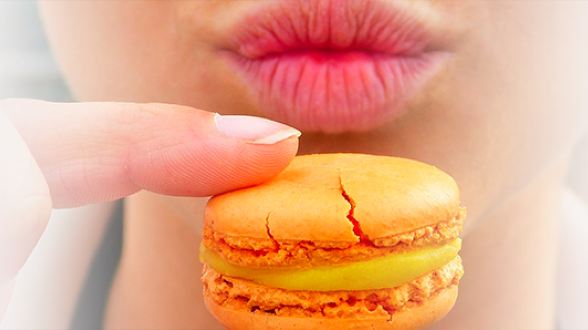 Widok dolnej części twarzy i ciasta przed nią trzymanego dwoma pacami prawej ręki. Ciastko z nadzieniem w środku.