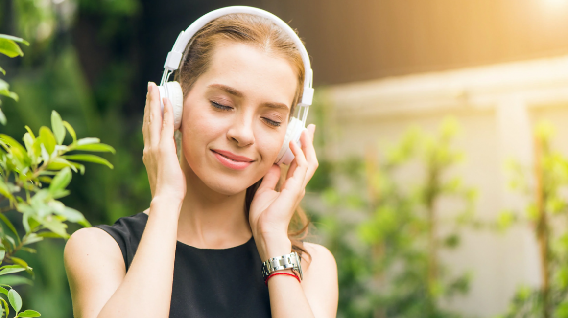 Uśmiechnięta dziewczyna z słuchawkami na uszach, na tle zieleni.