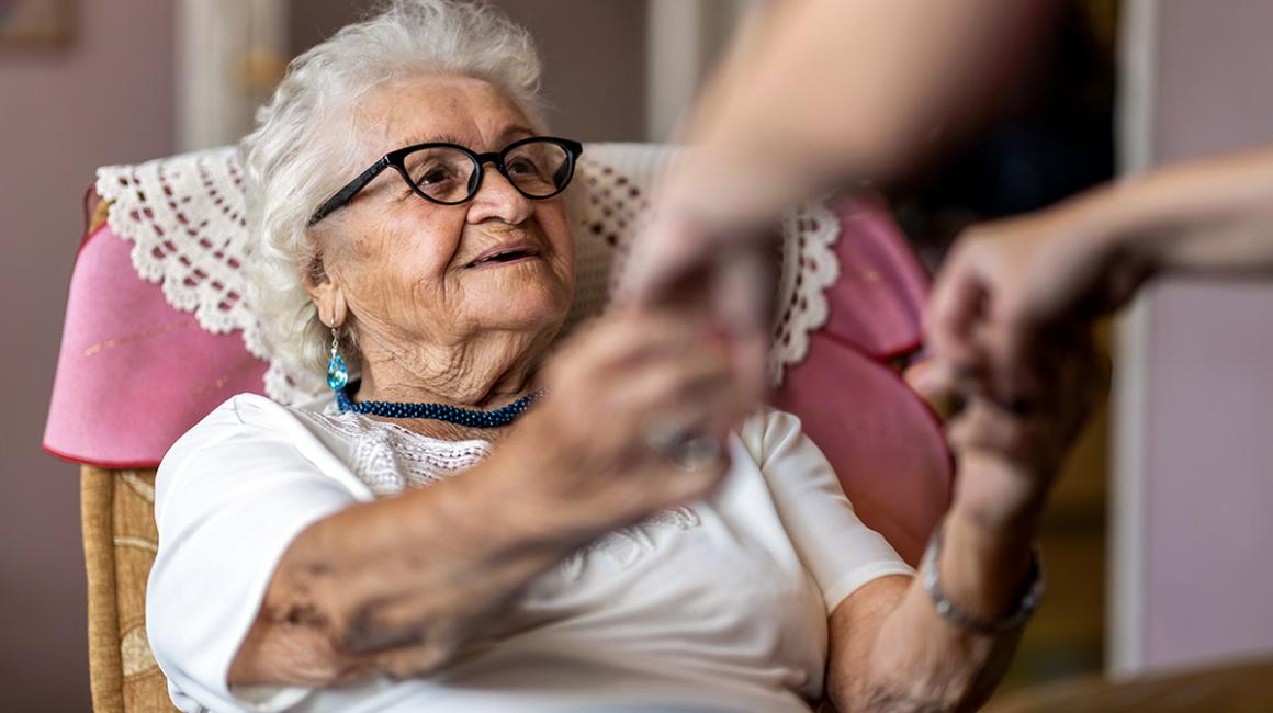 Starsza pani, której ktoś pomaga usiąść na łóżku