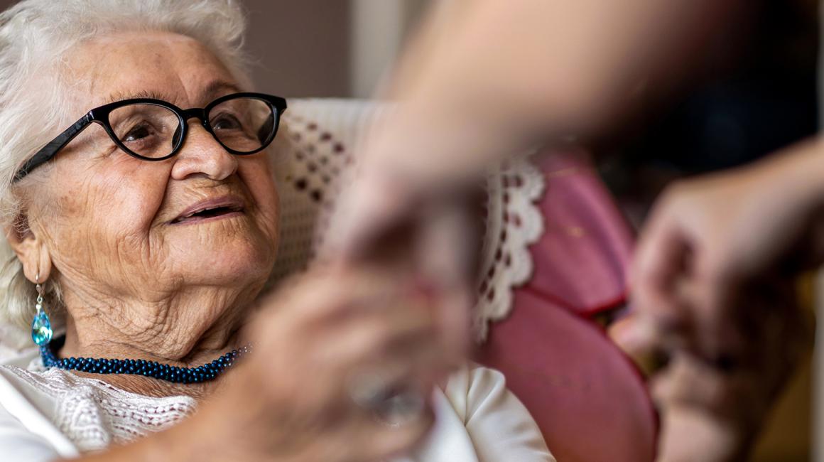 Starsza pani, której ktoś pomaga usiąść na łóżku