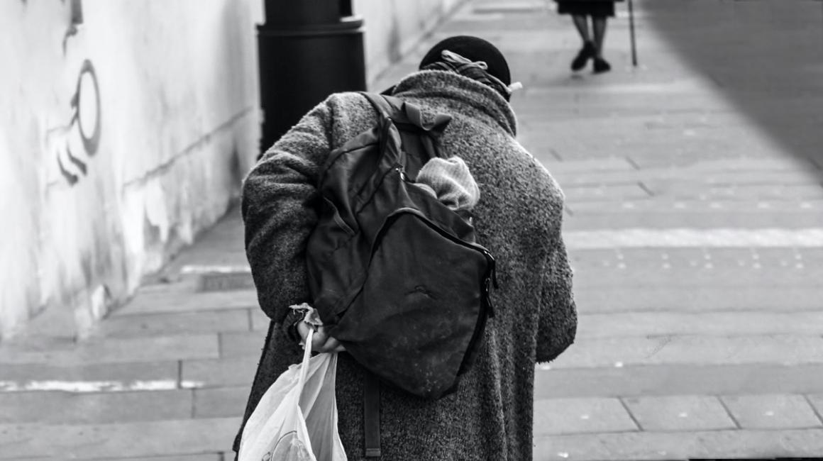 Bezdomna osoba z plecakiem i reklamówką, od tyłu, wchodząca po schodach
