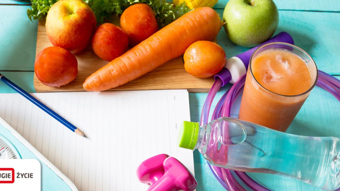 Leżące na deskach warzywa i owoce, waga, ciężarki, skakanka, szklanka z sokiem, kartka papieru