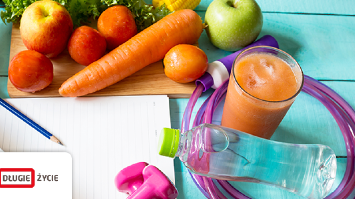 Leżące na niebieskich deskach warzywa i owoce, waga, ciężarki, skakanka, szklanka z sokiem, kartka papieru