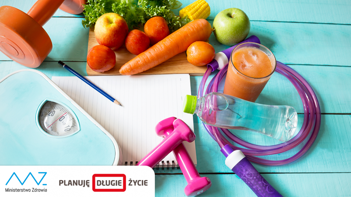 Leżące na niebieskich deskach warzywa i owoce, waga, ciężarki, skakanka, szklanka z sokiem, kartka papieru