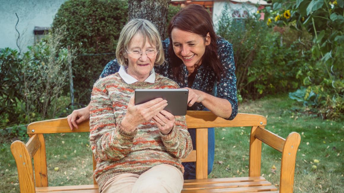 Dziewczyna pomaga zalogować się babci siedzącej na ławce w wiejskim ogródku