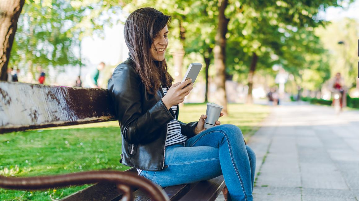 Kobieta na ławce w parku z telefonem w ręku, ekran z aplikacją obok
