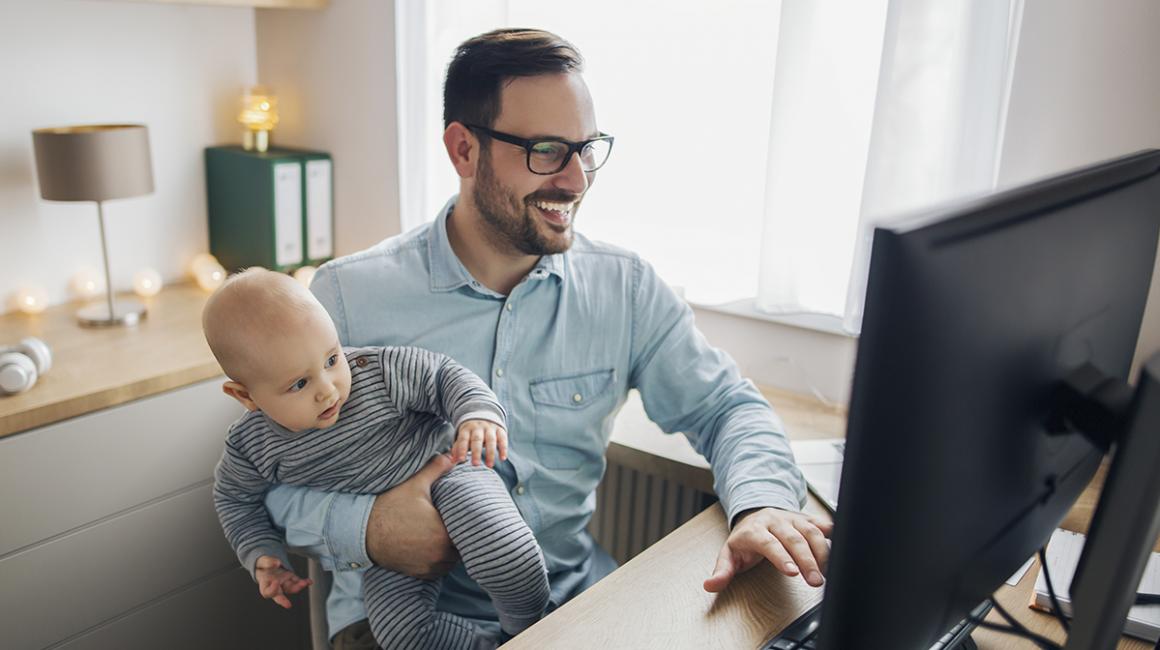 Tata z niemowlęciem na ręku przed komputerem