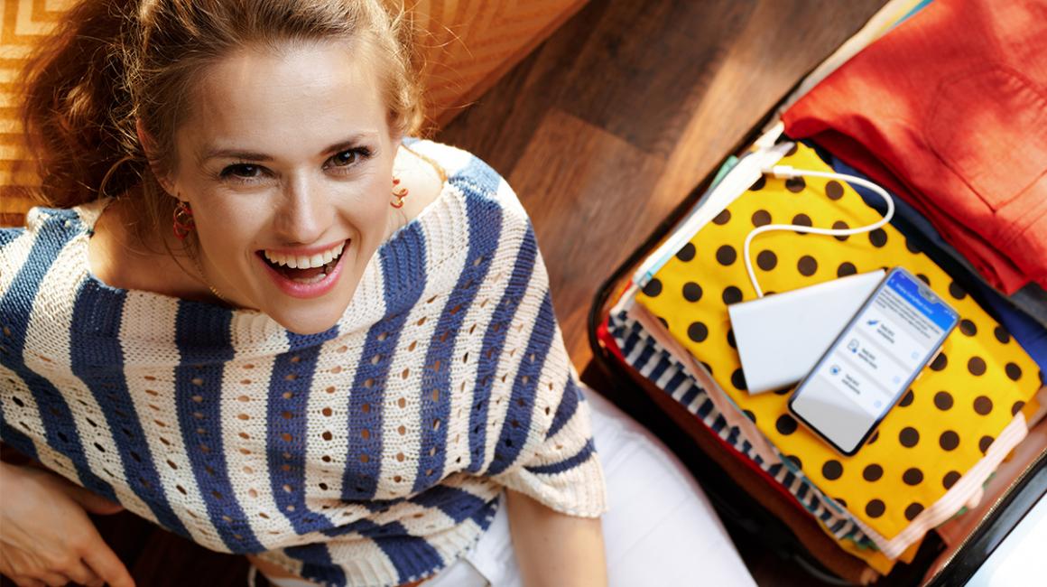 radosna kobieta, a na ubraniach w walizce leży komórka z UCC na ekranie