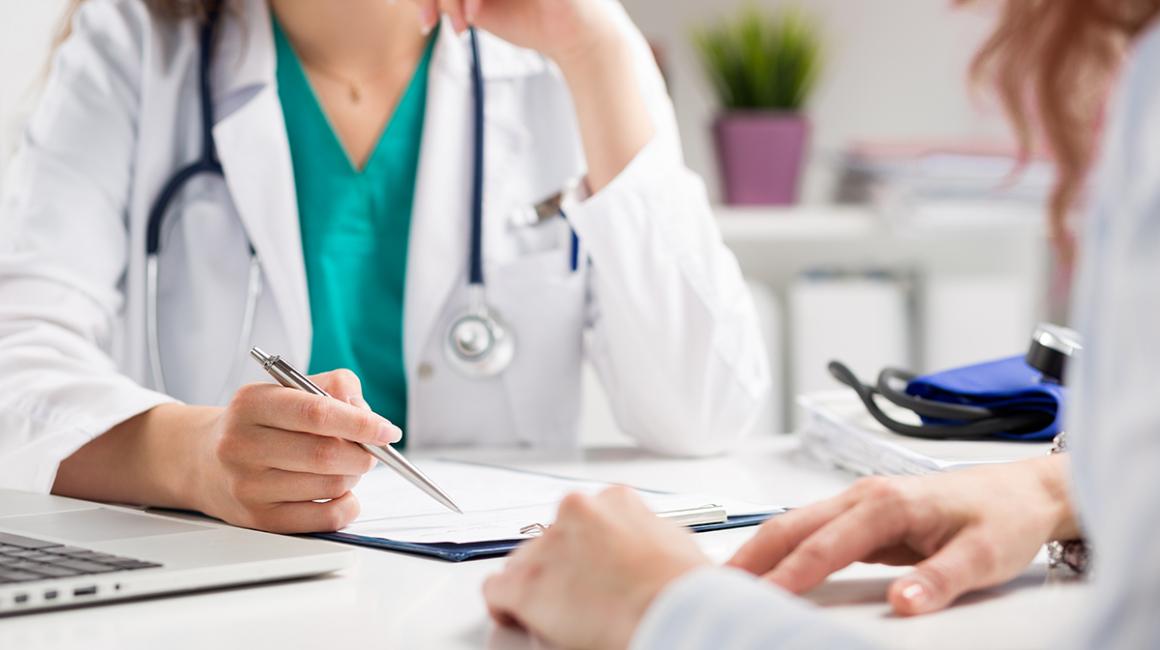 Lekarka z pacjentką siedzą przy stole. Na stole leżą dokumenty. 