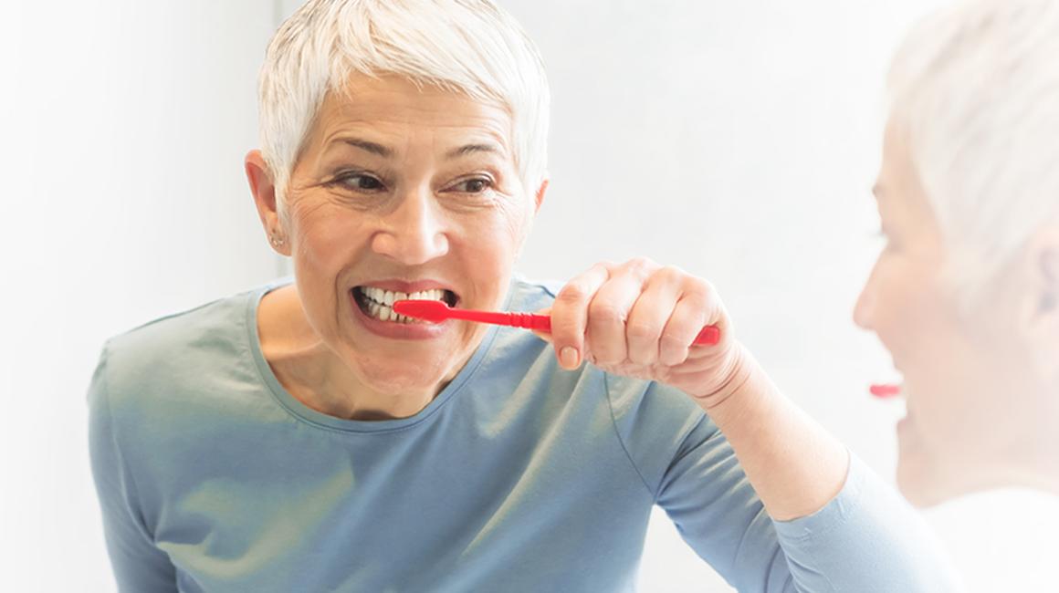 Odbicie w lustrze kobiety myjącej zęby.