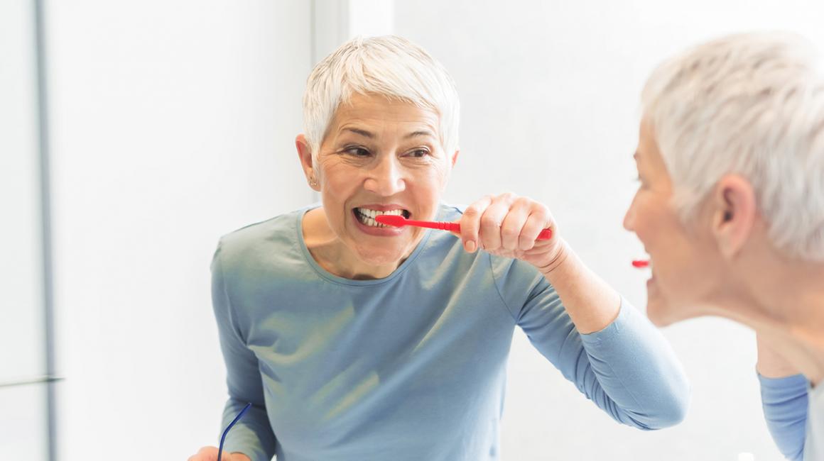 Odbicie w lustrze kobiety myjącej zęby.