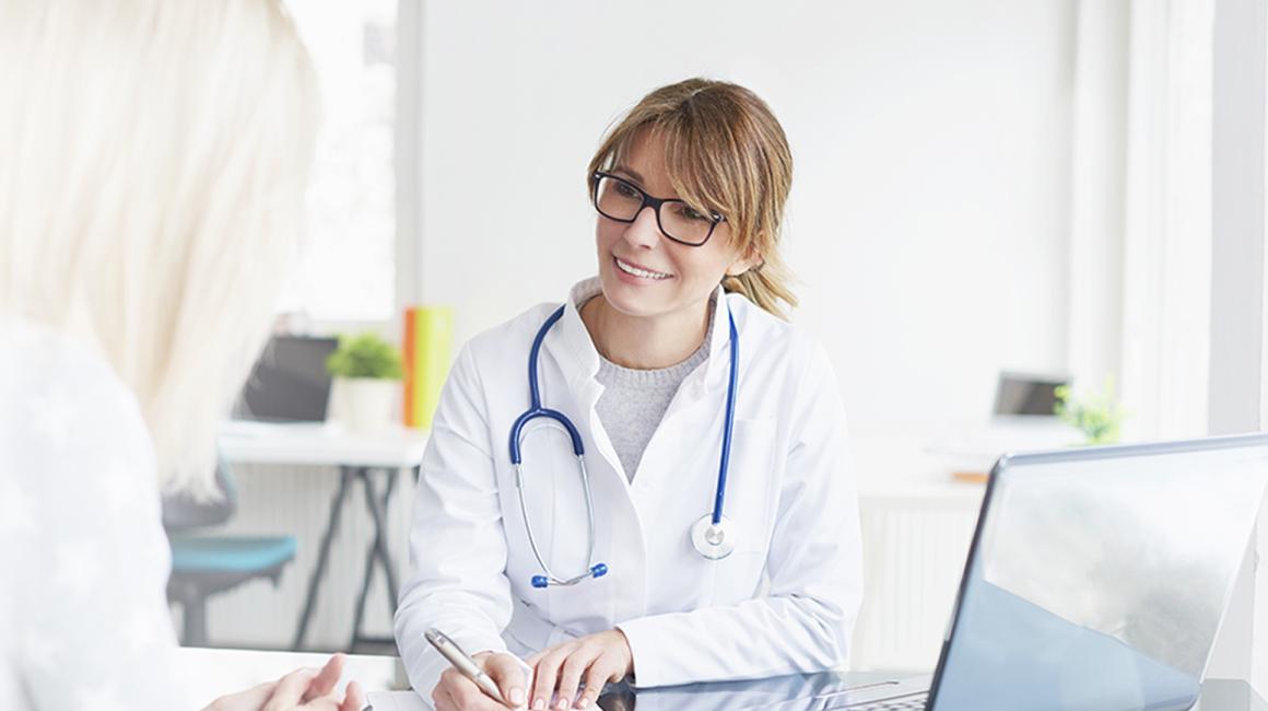 Siedząca lekarka rozmawiająca z pacjentką.