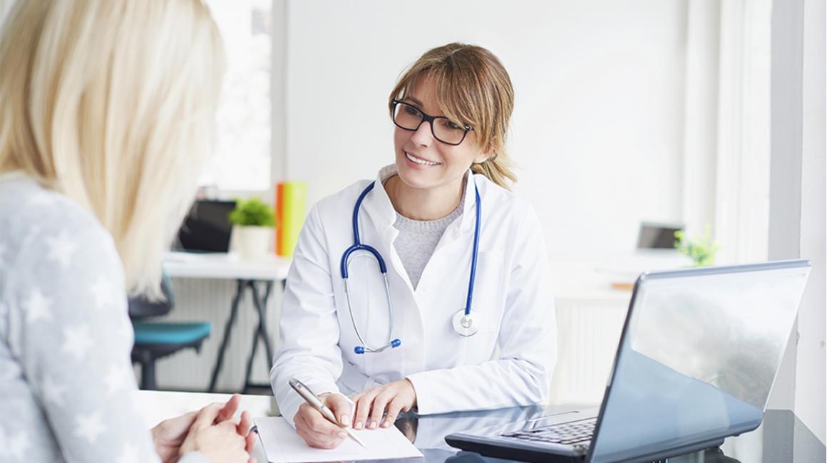 Siedząca lekarka rozmawiająca z pacjentką.