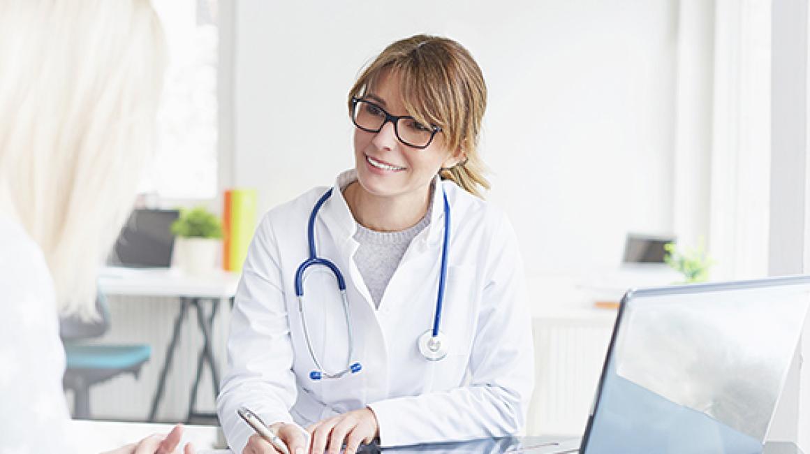 Siedząca lekarka rozmawiająca z pacjentką.