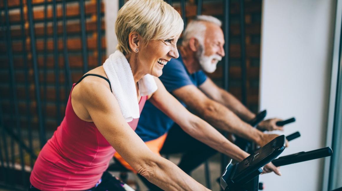 Starsza para ćwiczy na rowerkach stacjonarnych 