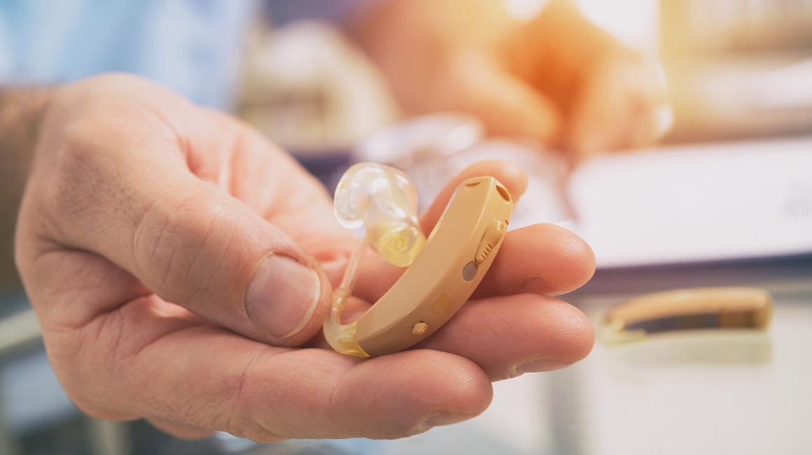 Wyciągnięta dłoń, na której leży aparat słuchowy