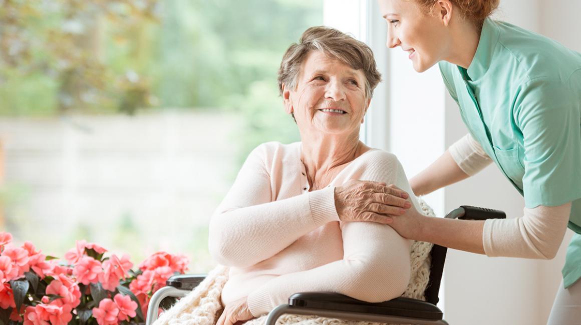 Uśmiechnięta starsza pani na wózku w towarzystwie młodej opiekunki