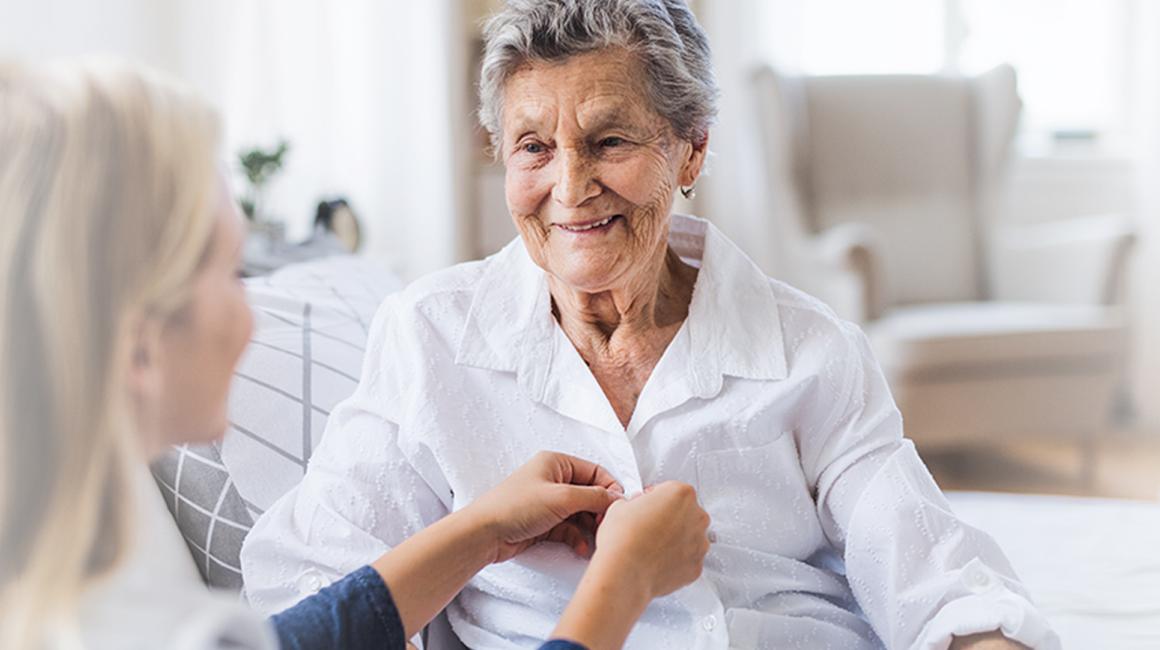 Młoda osoba pomaga się ubrać osobie starszej. Zapina guziki w jej koszuli zuli 