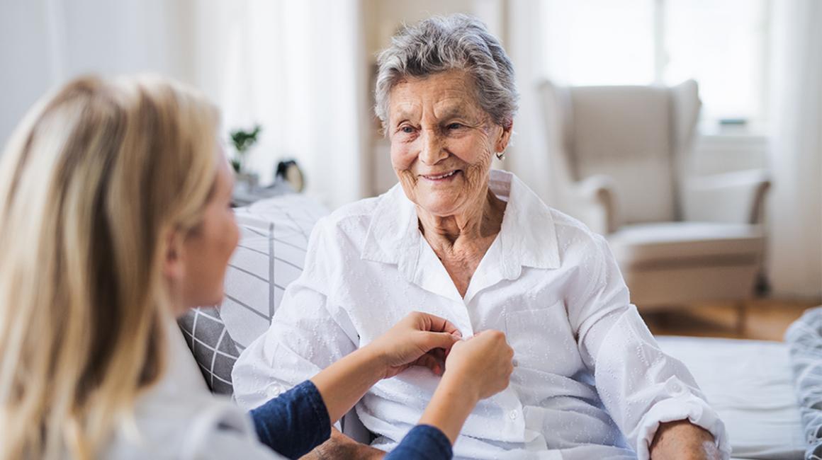 Młoda osoba pomaga się ubrać osobie starszej. Zapina guziki w jej koszuli zuli 