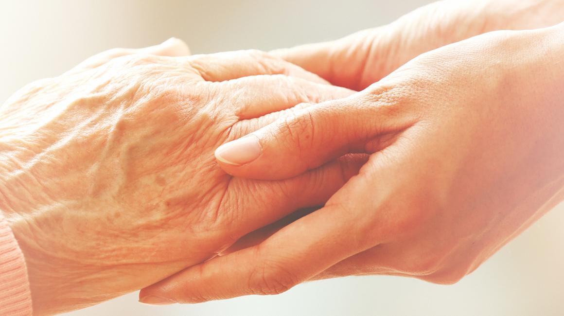 Zbliżenie na dłonie starszej osoby trzymane przez dłonie osoby młodszej