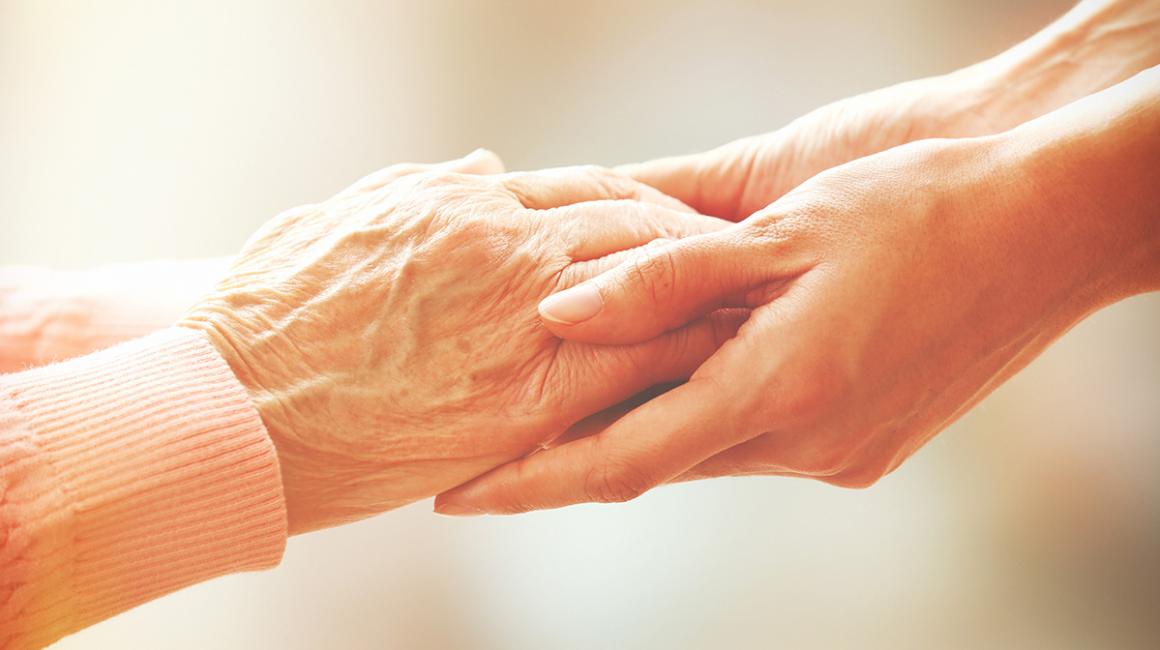 Zbliżenie na dłonie starszej osoby trzymane przez dłonie osoby młodszej