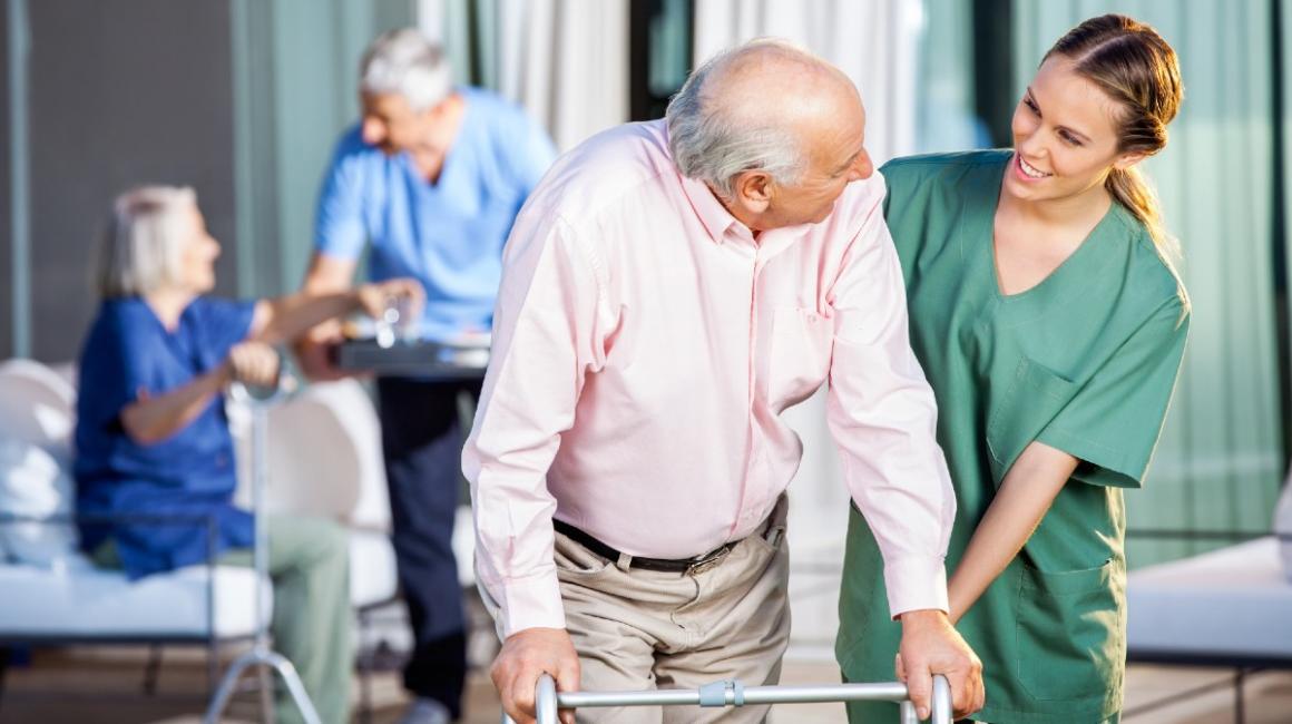 Starszy pan oparty o chodzik w asyscie pielęgniarki
