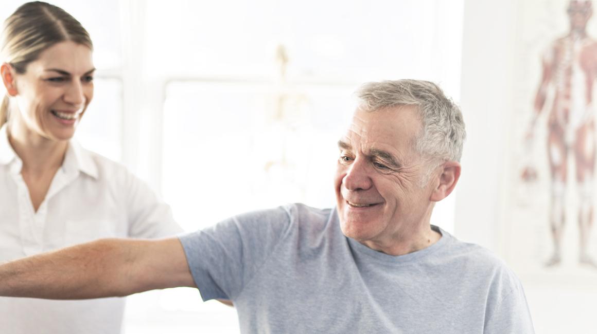 Starszy pan podnosi ciężarek z asystą fizjoterapeutki