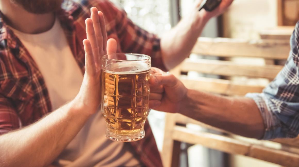 Mężczyzna podaje kufel z piwem koledze, ten odmawia dłonią blokując kufel.