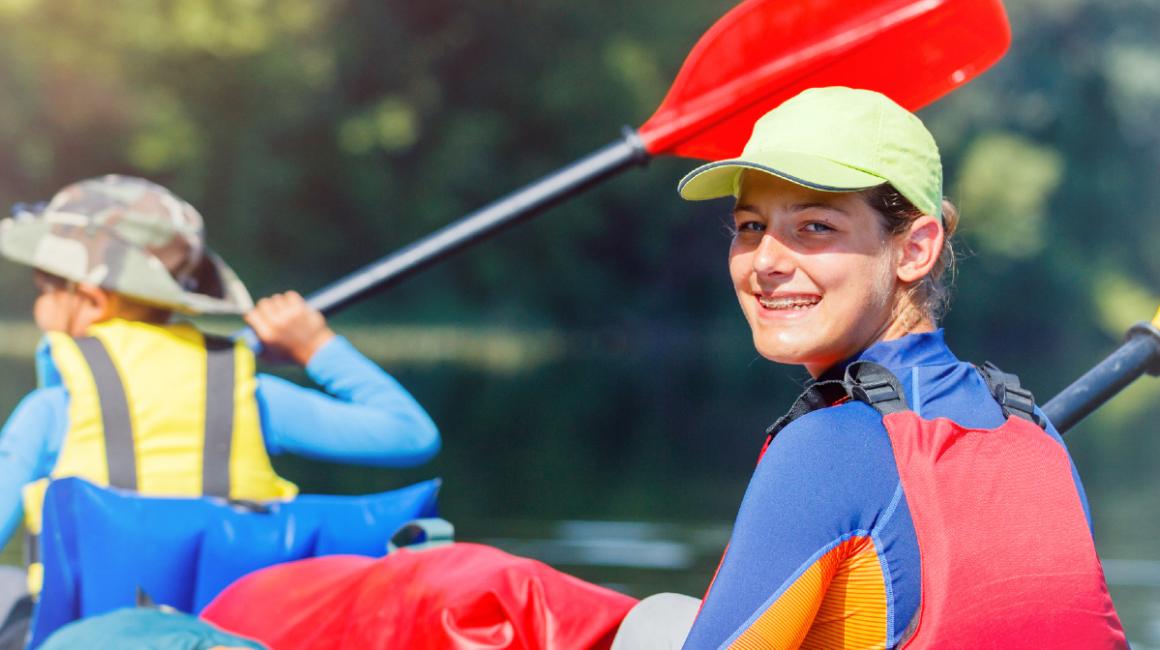 Uśmiechnięte dzieci ubrane w kamizelki ratunkowe płyną na rzece pontonem.