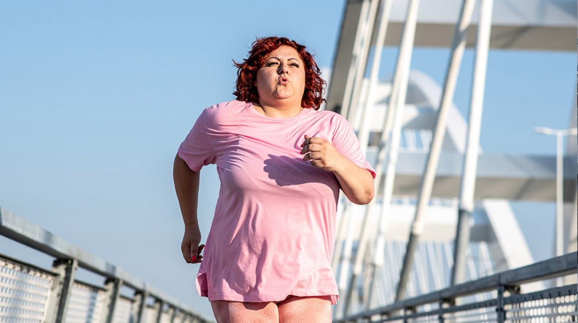 Biegnąca kobieta z nadwagą. W tle nowoczesny most