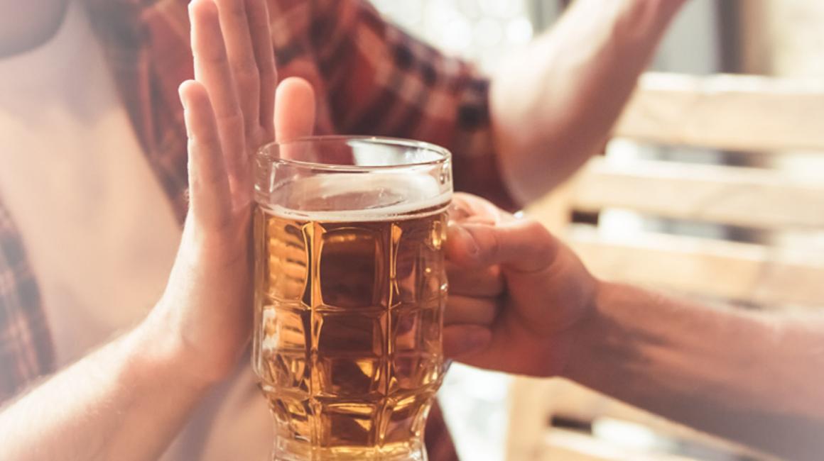 Mężczyzna podaje kufel z piwem koledze, ten odmawia dłonią blokując kufel.