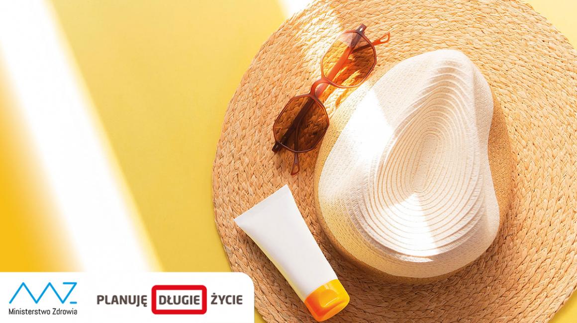 Na słomkowy kapelusz, na nim okulary i krem do opalania padają promienie słońca.