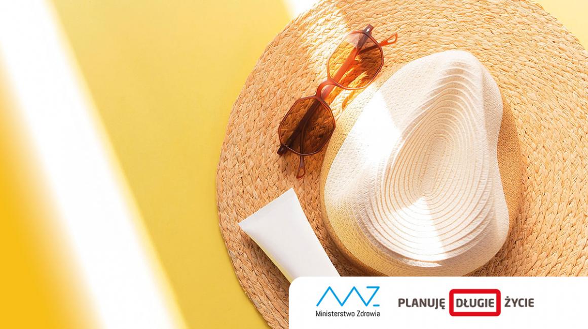 Na słomkowy kapelusz, na nim okulary i krem do opalania padają promienie słońca.