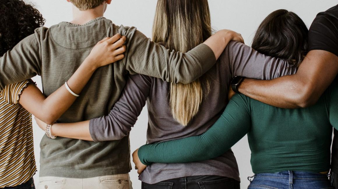 Cztery osoby stoją tyłem i obejmują się ramionami. 