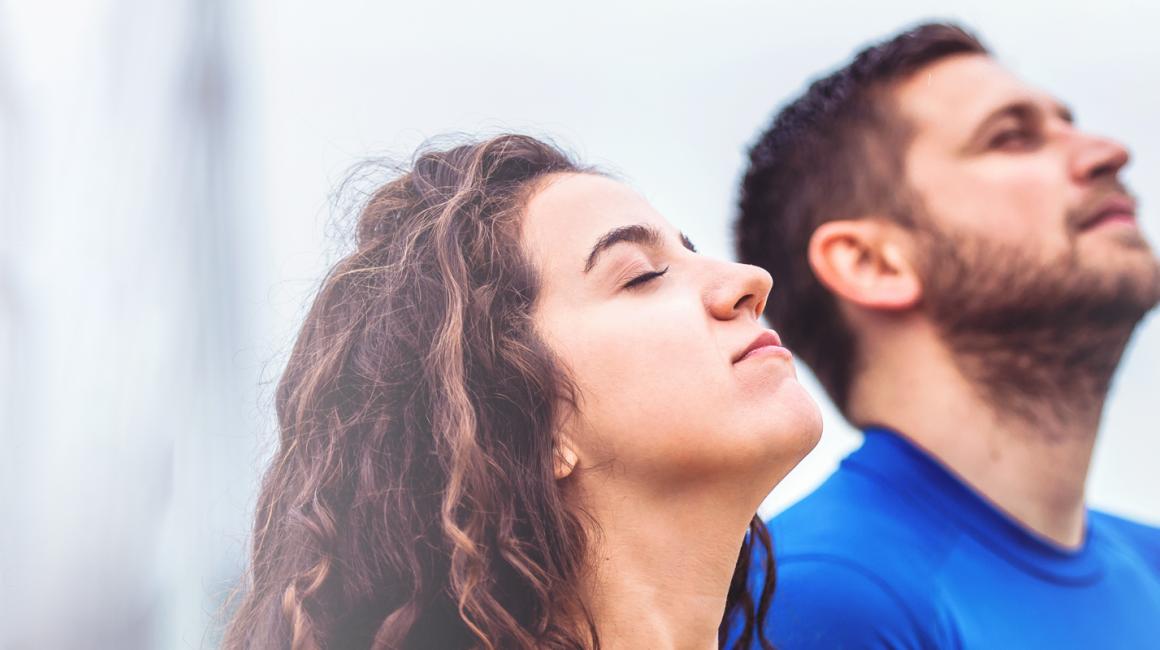 Młodzi kobieta i mężczyzna stoją z głowami skierowanymi ku niebu i oddychają pełną piersią świeżym powietrzem.