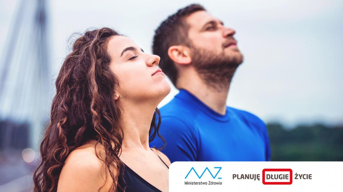 Młodzi kobieta i mężczyzna stoją z głowami skierowanymi ku niebu i oddychają pełną piersią świeżym powietrzem.