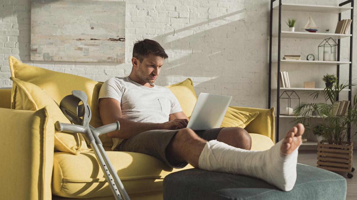 Mężczyzna z nogą w gipsie z komputerem na kolanach