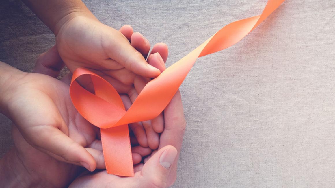 Pomarańczowa  wstążka leży na dłoniach dziecka, a one leżą na dłoniach dorosłej osoby
