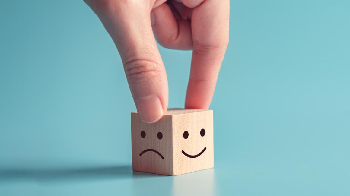 Drweniana kostka, na jednej ściance jest smutna buźka, na drugiej uśmiechnięta.