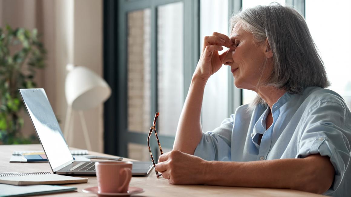 Kobieta przy laptopie, uciskająca jedną ręką oczy.