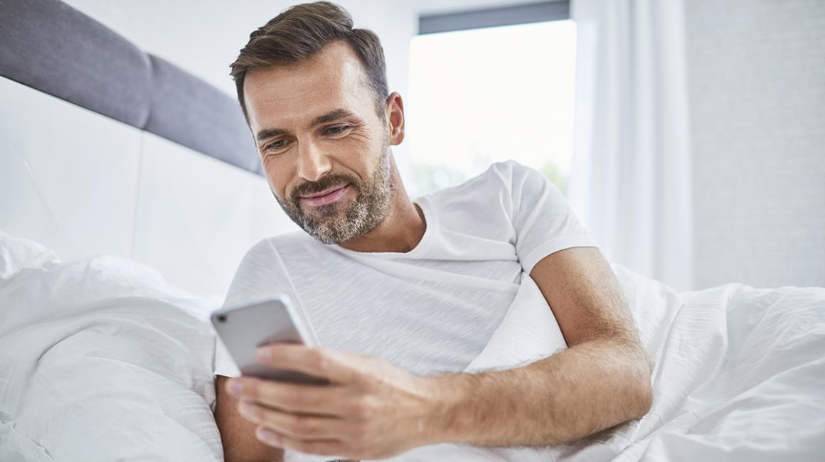 Leżący w łóżku facet patrzy na swój telefon