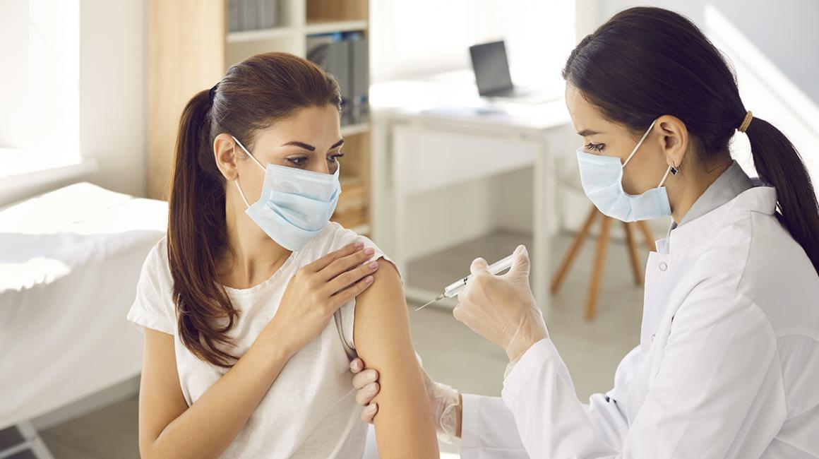 Pielęgniarka wykonuje kobiecie zastrzyk, obie w maseczkach