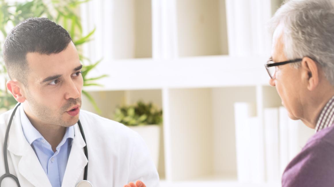 Siedzą lekarz i bokiem starszy pan. Lekarz coś tłumaczy