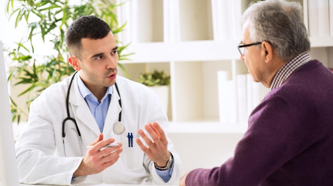 Siedzą lekarz i bokiem starszy pan. Lekarz coś tłumaczy