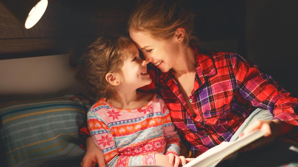 Uśmiechnięte młoda matka i córka w wieku wczesnoszkolnym. Siedzą i wspólnie czytają książkę.