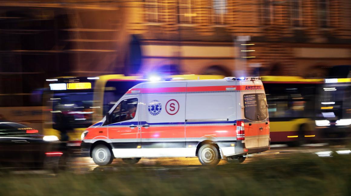 Karetka na sygnale jedzie ulicą w nocy. 